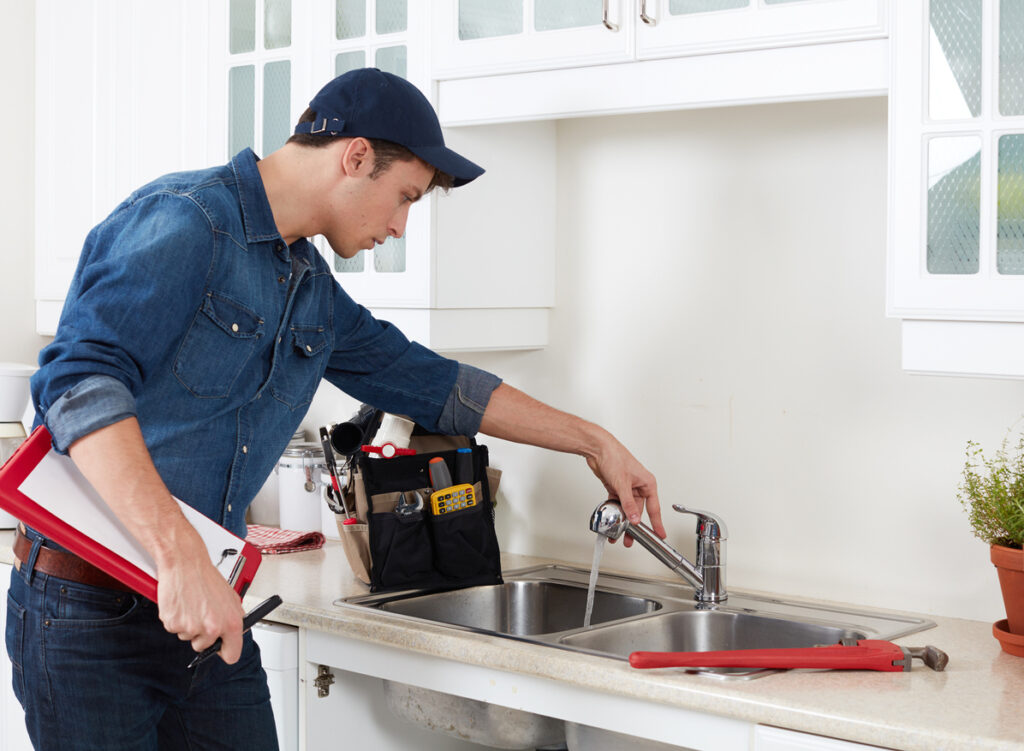Professional plumber holding clipboard and testing kitchen sink in apartment unit